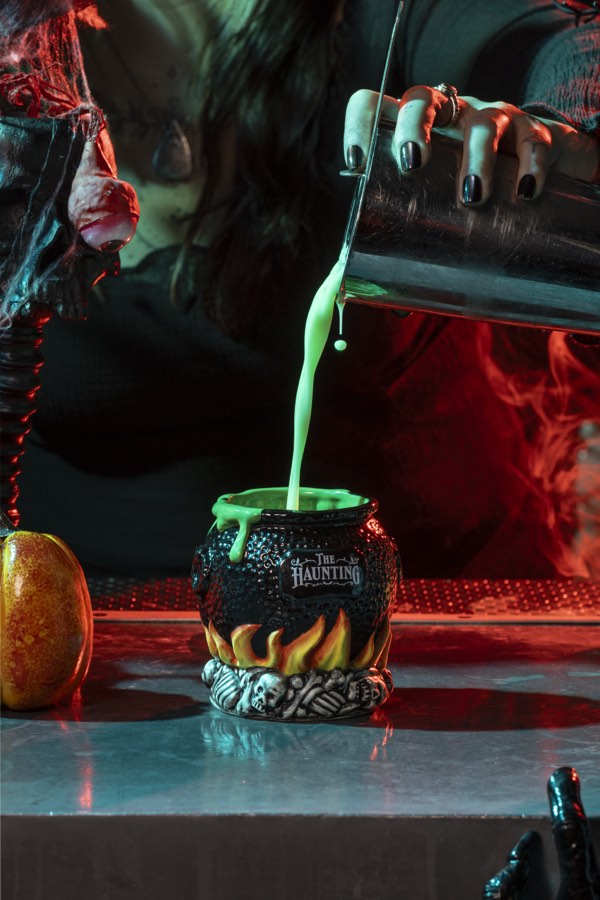 A black cauldron mug on a bed of flames being filled with bright green cocktail.