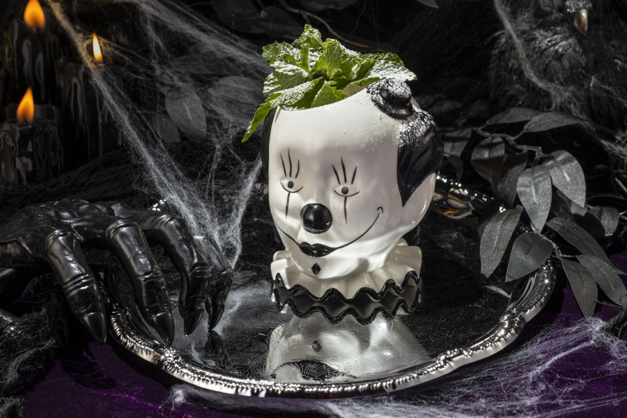A white ceramic clown-head mug garnished with mint, lit in purple.
