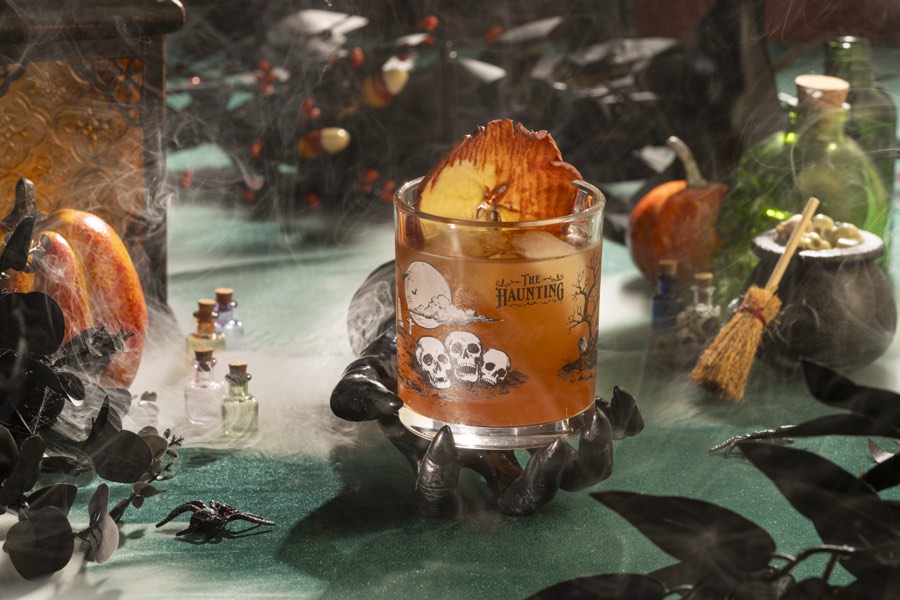 A deep red rocks cocktail surrounded by dark roses and candlelight.