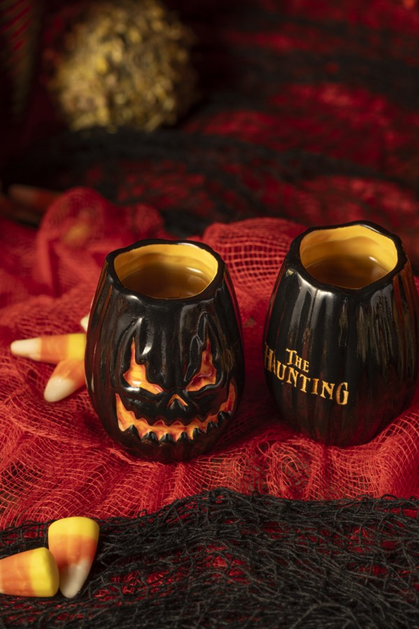 Two carved jack-o-lantern shot glasses on red velvet.