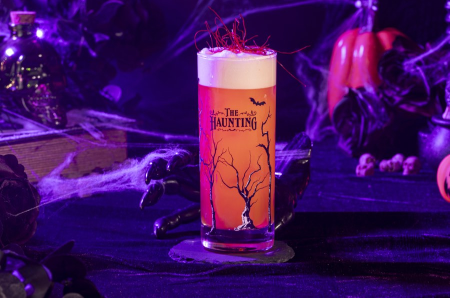 A pale orange layered collins cocktail against violet smoke.
