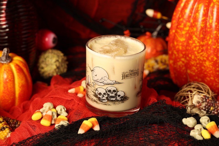 A rocks cocktail lit in teal and red among Halloween decor.
